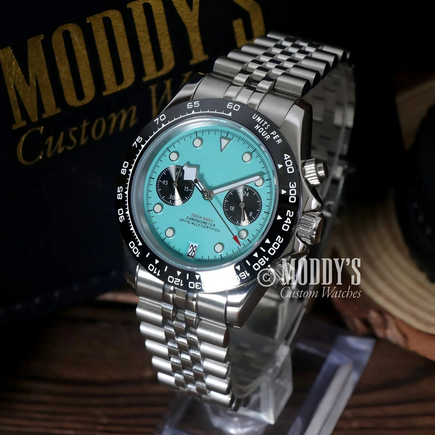 Silver chronograph wristwatch with turquoise face featuring Seiko VK63 hybrid movement