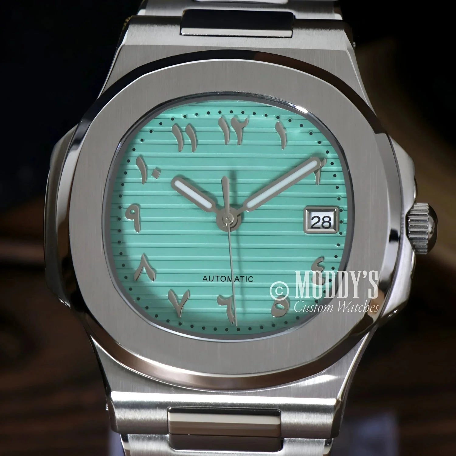 Silver wristwatch with turquoise face and Arabic numerals, featuring Seiko NH35 automatic