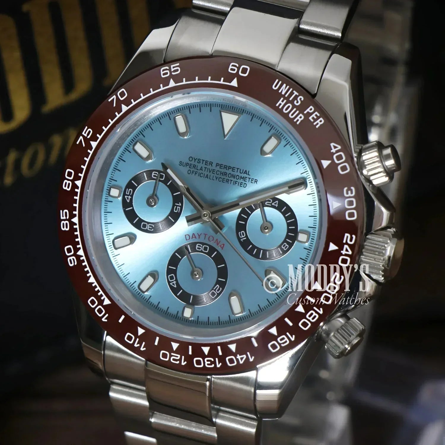 Silver Rolex Daytona watch with blue face, brown bezel, featuring Seiko VK63 hybrid movement