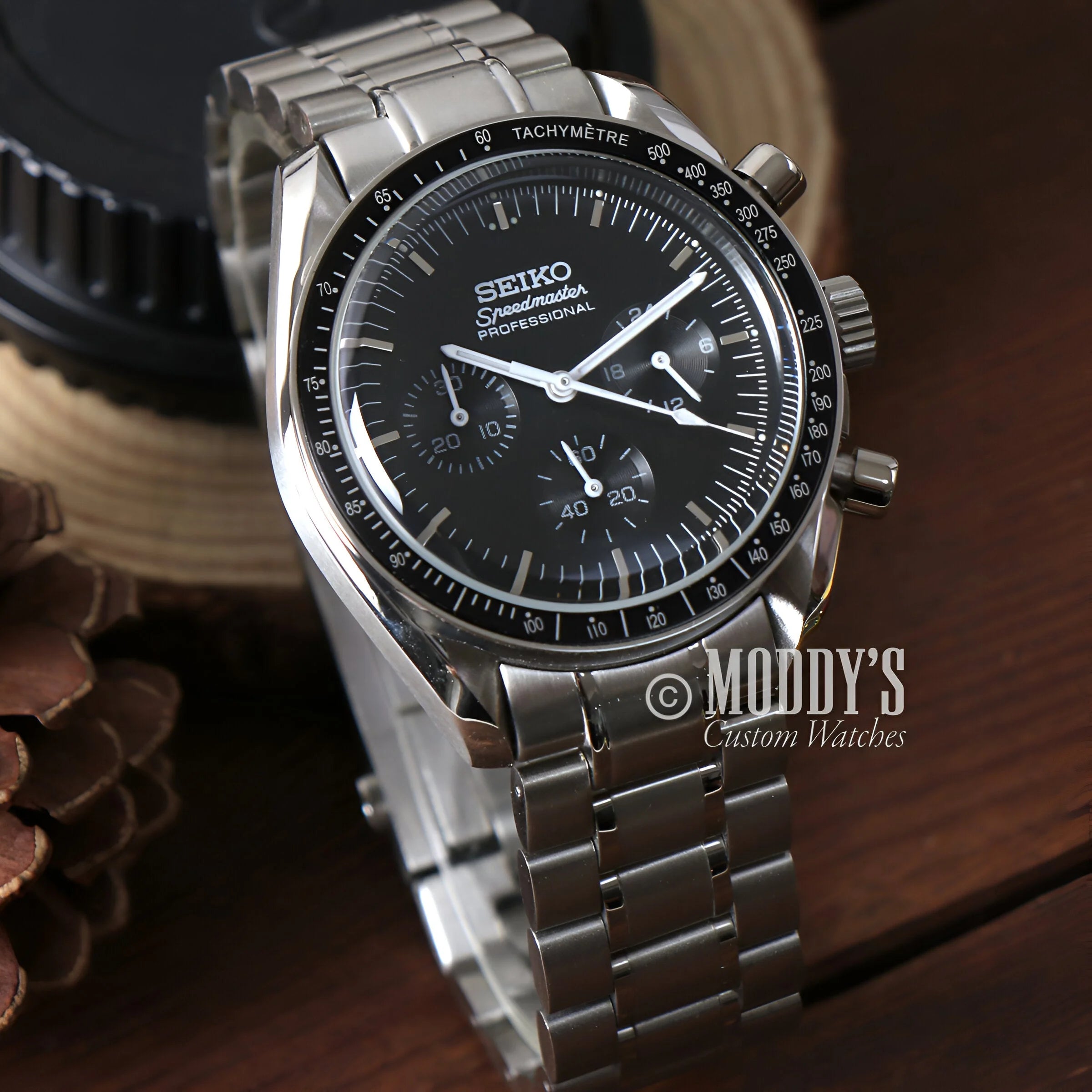 A Close-up Of The Speedseiko Black Watch On a Table With Pine Cones, Seiko Mod Speedmaster