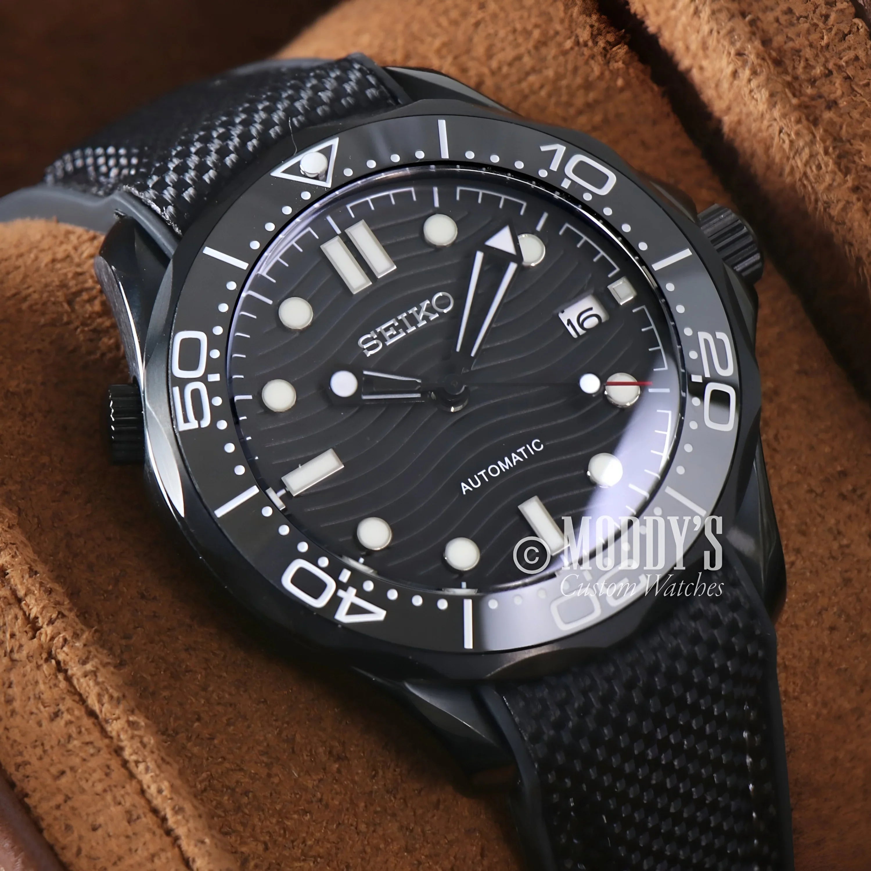 Close-up Of Seikomaster Full Black Watch With Black Strap On Brown Cloth, Featuring Nh35 Automatic